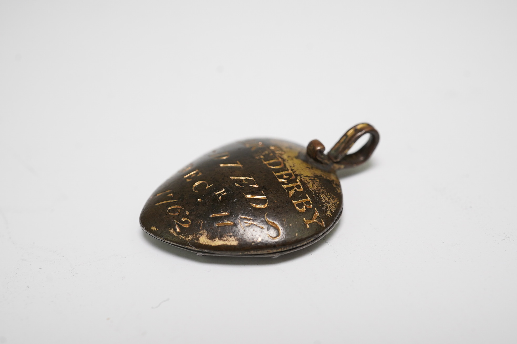 An 18th century gilt metal heart shaped mourning pendant, with engraved inscription, 'CARna DERBY DIED DEC 11th, 1762' and plaited hair beneath a glazed panel verso, 27mm.